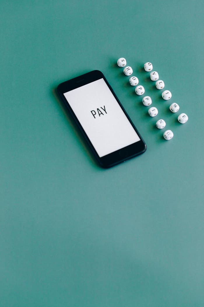 Smartphone with PAY text next to beads on green background, symbolizing online payment.