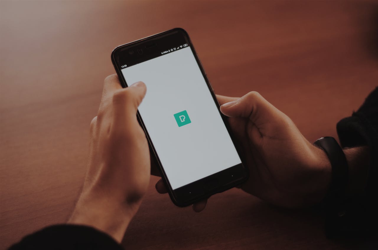 Person holding a smartphone displaying a blank screen with a logo in a cozy indoor setting.